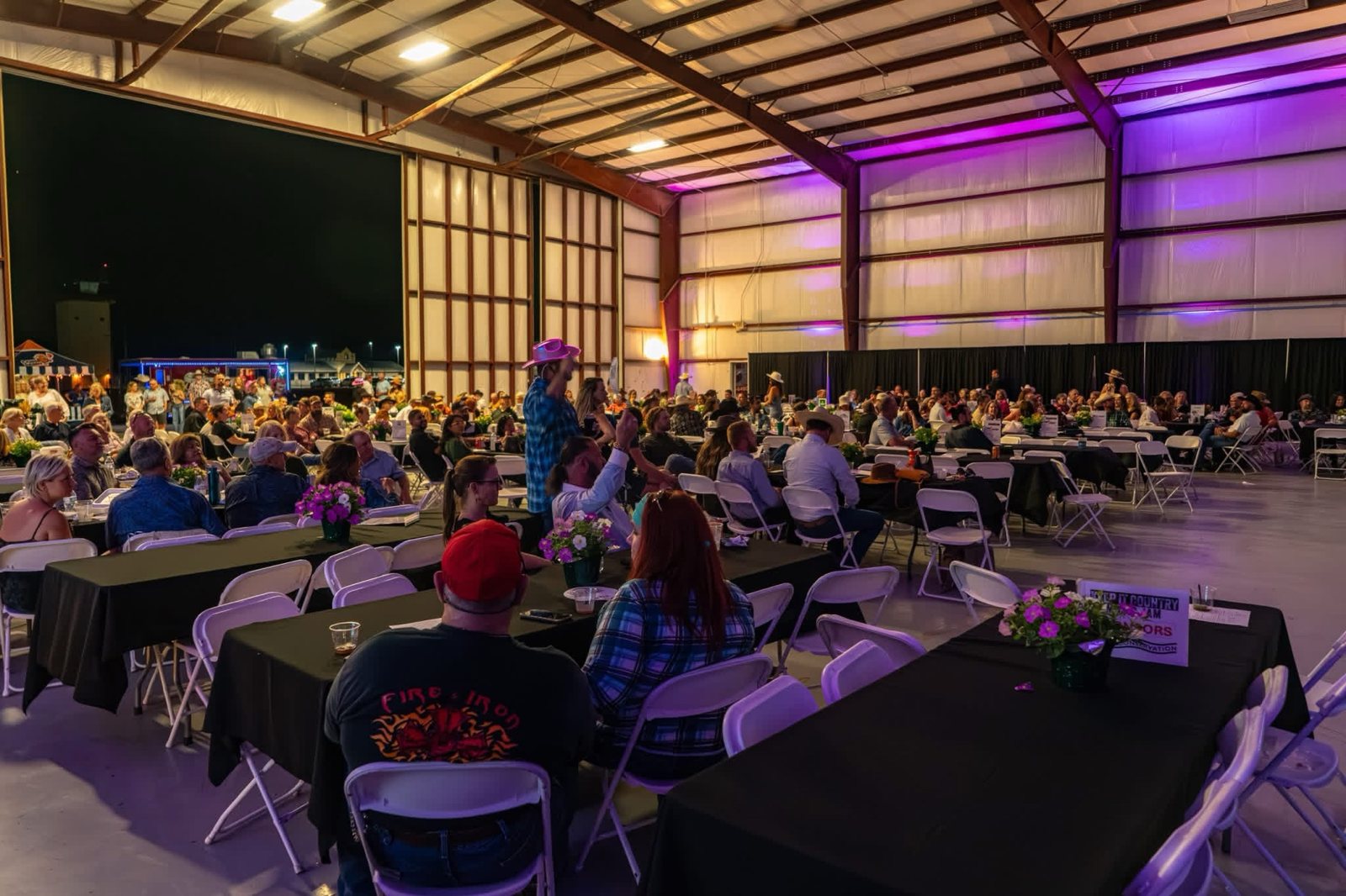 A packed hangar of guests at the Hill Country Music Jam benefit, cheering under purple stage lighting