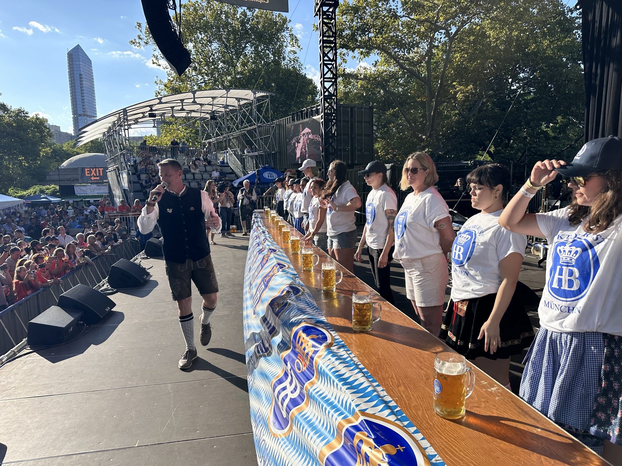 Stein-holding competitors lined up behind full steins on the Central Park Oktoberfest stage